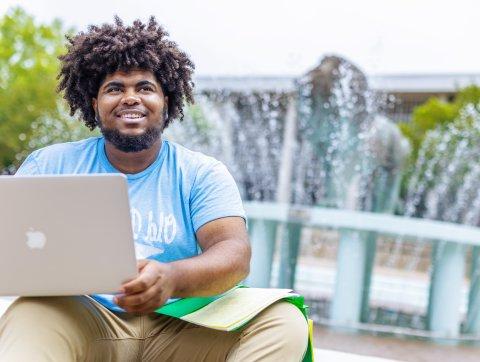 student sitting at the base of the lion fountain smiling